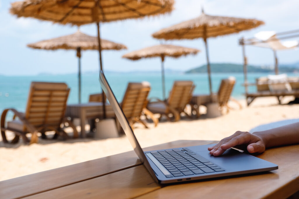 Remote worker with laptop at beach resort. Searching for the best travel insurance for digital nomads.